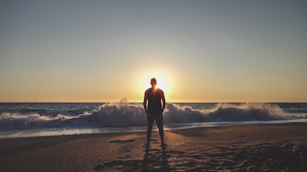 Man standing on a beach looking at the sunset. 